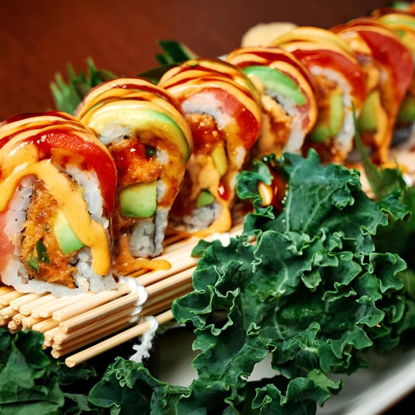 Pink Basil's Asian-fusion sushi rolls with avocado, tuna, and sauces on a bamboo mat with kale.