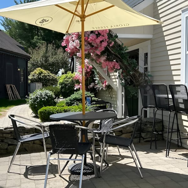 Outdoor patio with a table, chairs, umbrella, and pink flowers, next to a white building.