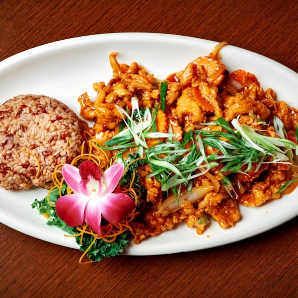 Pink Basil's orange chicken with brown rice, garnished with a pink orchid and shredded carrots.