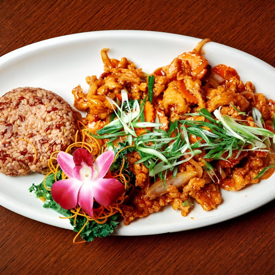 Pink Basil's orange chicken with brown rice, garnished with a pink orchid and shredded carrots.