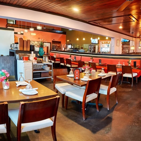 Pink Basil restaurant interior with dining tables, red booth seating, and a bar area.