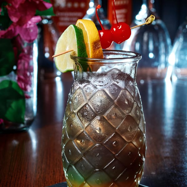 A Pink Basil cocktail in a textured glass, garnished with lime, lemon, and cherries.