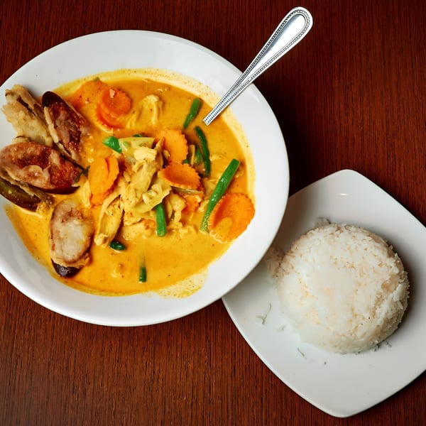 Pink Basil's red curry with chicken, vegetables, and sausage, served with a side of white rice.